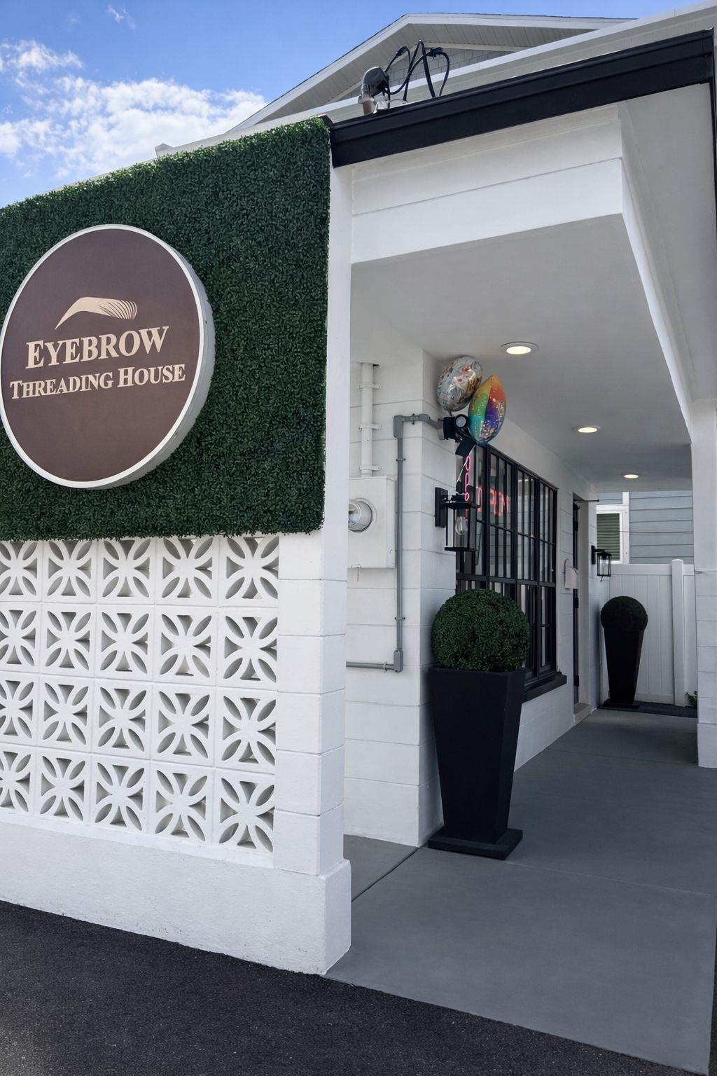 The Eyebrow Threading House storefront on South MacDill Avenue, with its round sign on a boxwood hedge wall